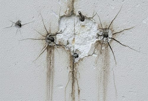 Detail poškozené fasády s prasklinami kolem neodborně provedeného kotvení ocelového prvku.