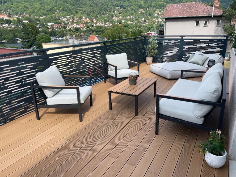 Zábradlí Moderní ocelová terasa s designovým kovovým zábradlím, WPC podlahou a venkovním nábytkem s výhledem do údolí.