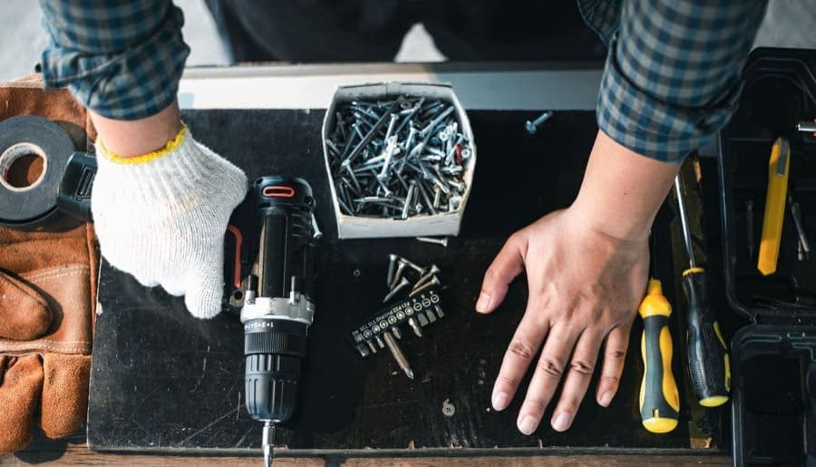 Zakázková výroba a montáž ocelových konstrukcí | KOVOSET Detailní záběr na řemeslníka při montáži ocelové konstrukce s aku vrtačkou a spojovacím materiálem.